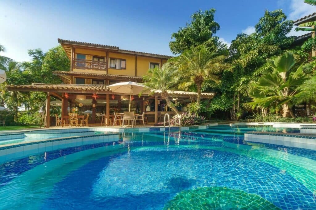 Piscina a frente do Hotel Via dos Corais durante o dia e ao fundo a estadia. Representa airbnb na Costa do Sauípe