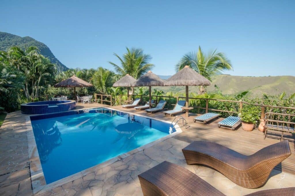 Vista da piscina da Ilha de Toque Toque Boutique Hotel & Spa durante o dia com cadeiras do lado direito da imagem no centro a piscina de adulto e ao fundo uma piscina de criança.