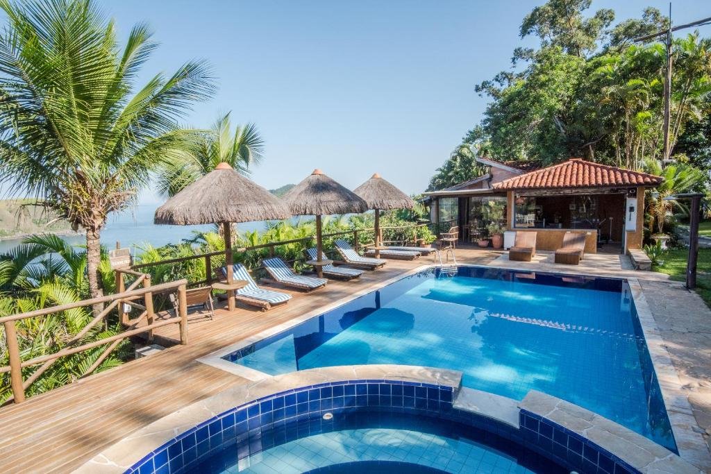 Um resort tropical dispõe de piscina, espreguiçadeiras e guarda-sóis de palha com vista para o oceano e a vegetação ao redor. Esse é o Ilha de Toque Toque Eco Boutique Hotel & Spa.