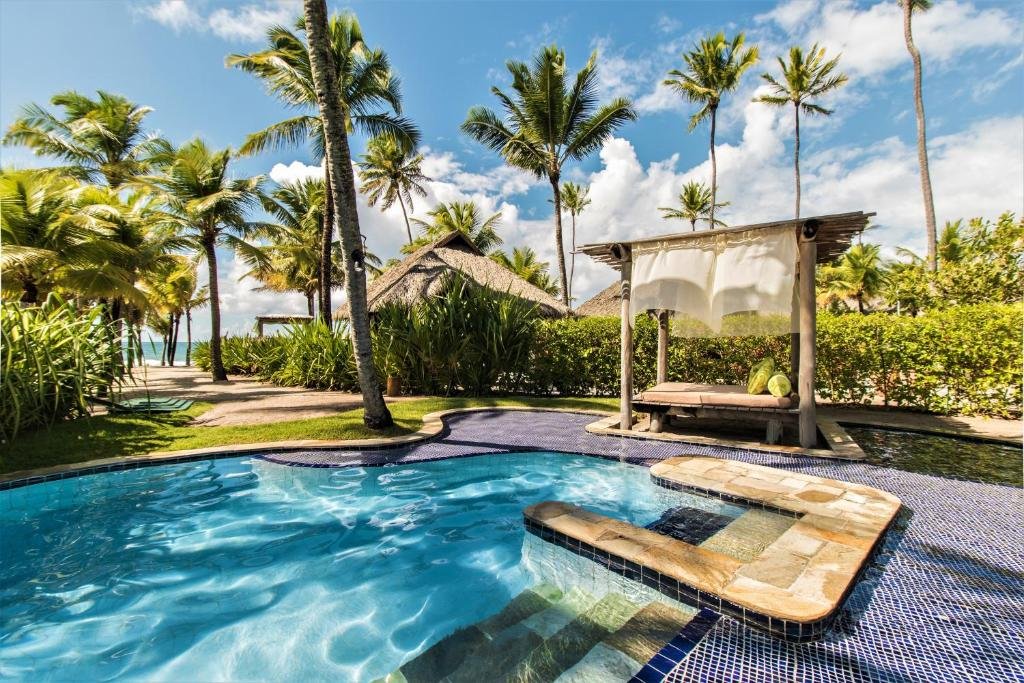 Uma piscina tropical no NANNAI Muro Alto com águas azuis cristalinas, cercada por palmeiras e vegetação, com uma área de descanso na sombra.