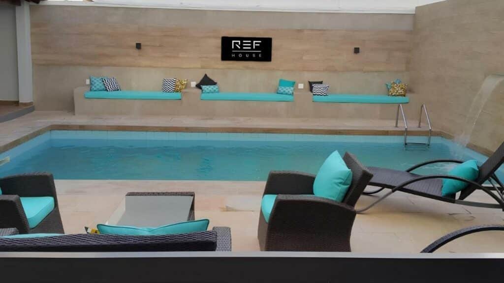 Piscina ao ar livre do Hygge House na Barra da Tijuca durante o dia com sofá a frente ao meio a piscina.