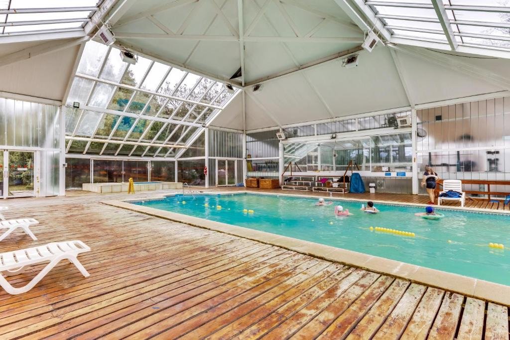 Piscina coberta do Selina Bariloche com cadeiras perto, quatro pessoas dentro da piscina com boias e uma pessoa do lado esquerdo andando.