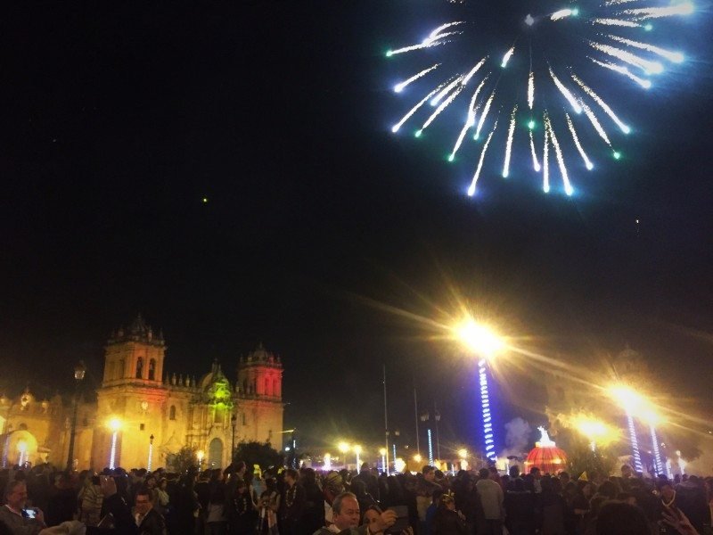 Virada do ano na Plaza de Armas com fogos de artifício no céu e uma grande multidão reunida. Prédios são iluminados com luzes coloridas. Imagem para ilustrar post sobre réveillon em Cusco.