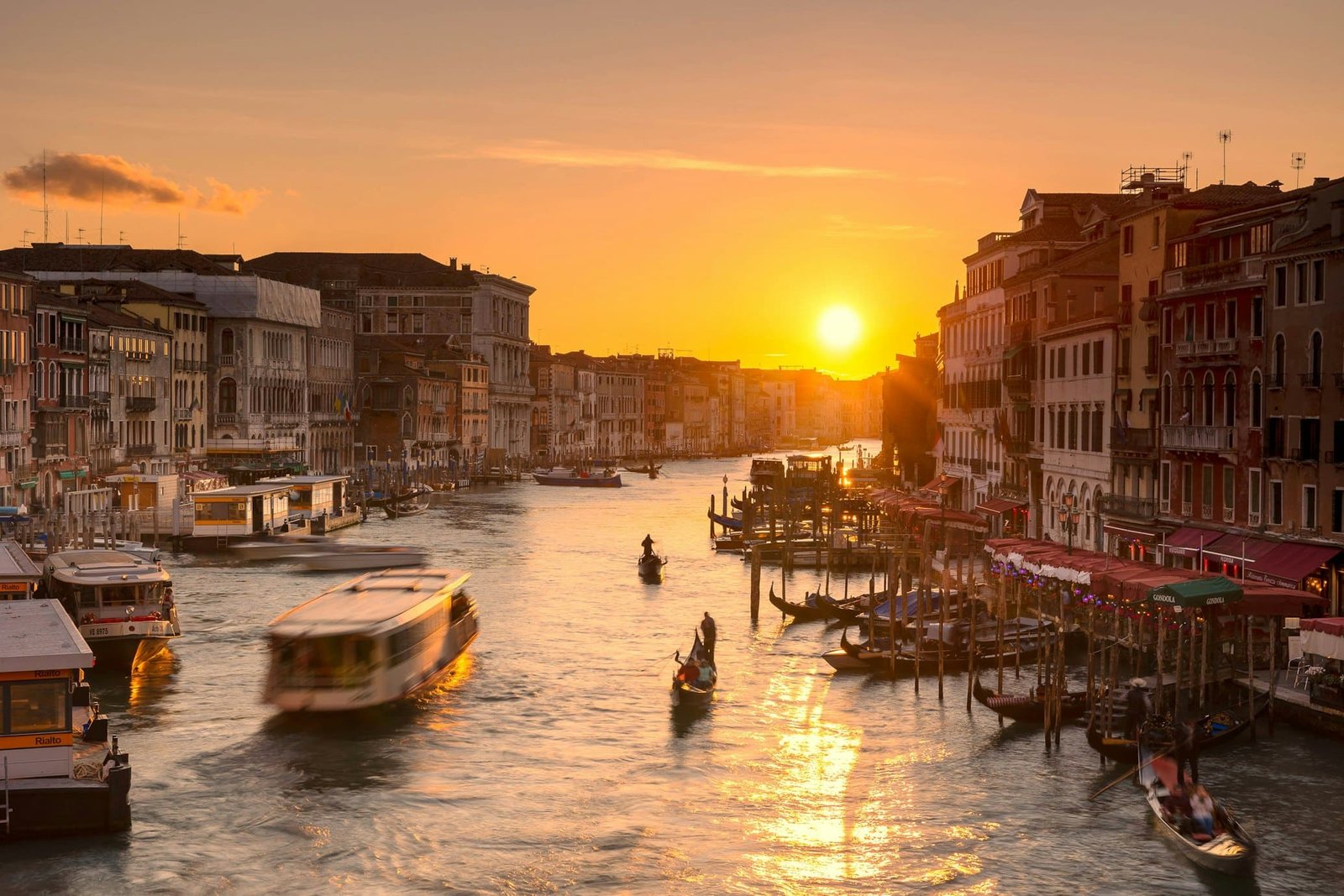 Pôr do sol sobre o Grande Canal em Veneza, com barcos na água e edifícios históricos ao longo do canal.