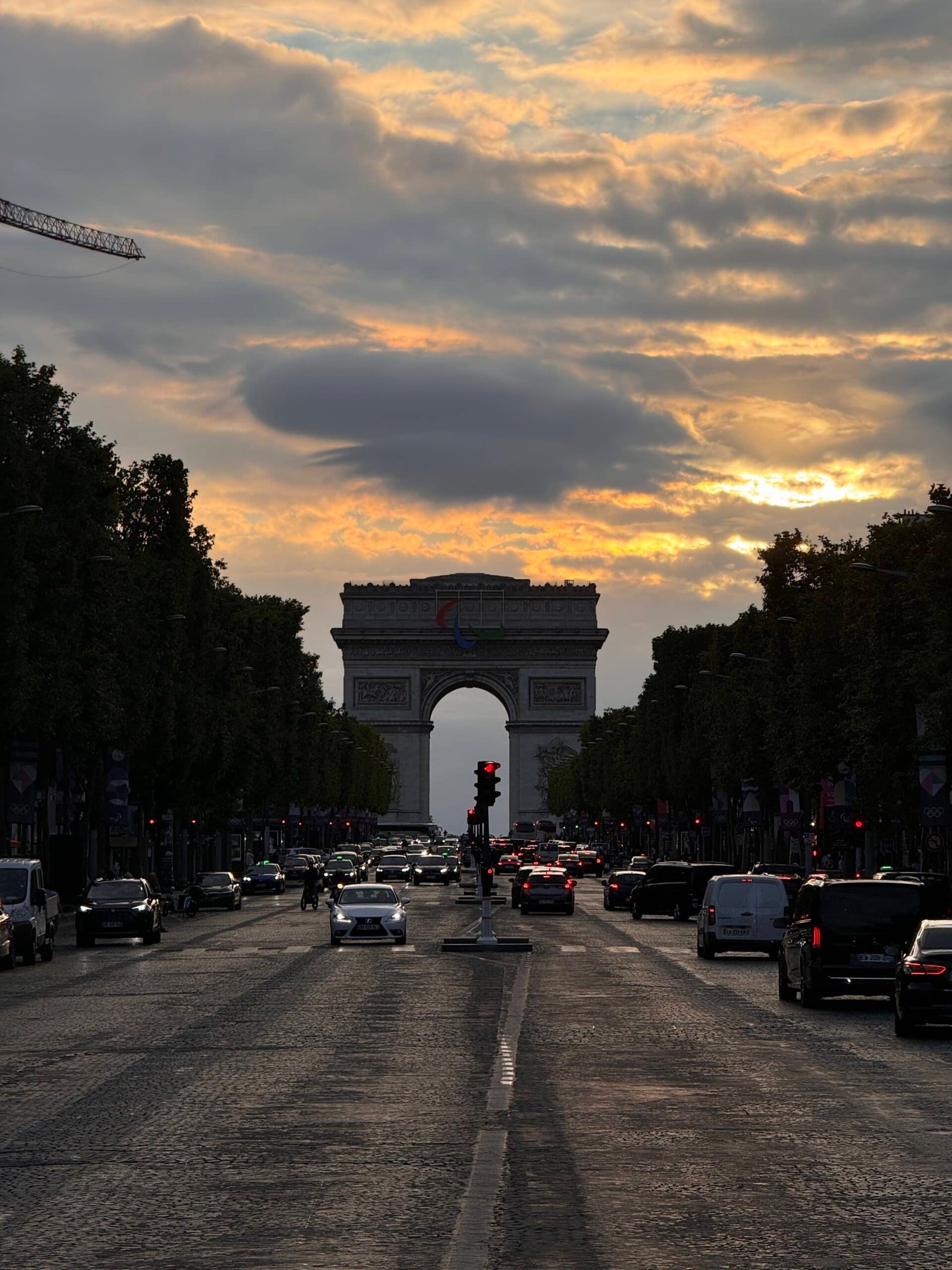 Uma vista do pôr do sol no Arco do Triunfo com carros e árvores ao longo da rua em uma rua movimentada de Paris, a Champs-Elysées.