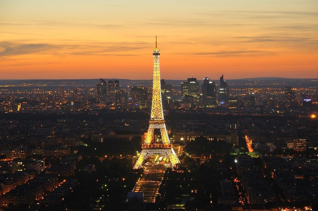 A Torre Eiffel iluminada à noite com o horizonte da cidade ao fundo, contrastando com o céu do pôr do sol.