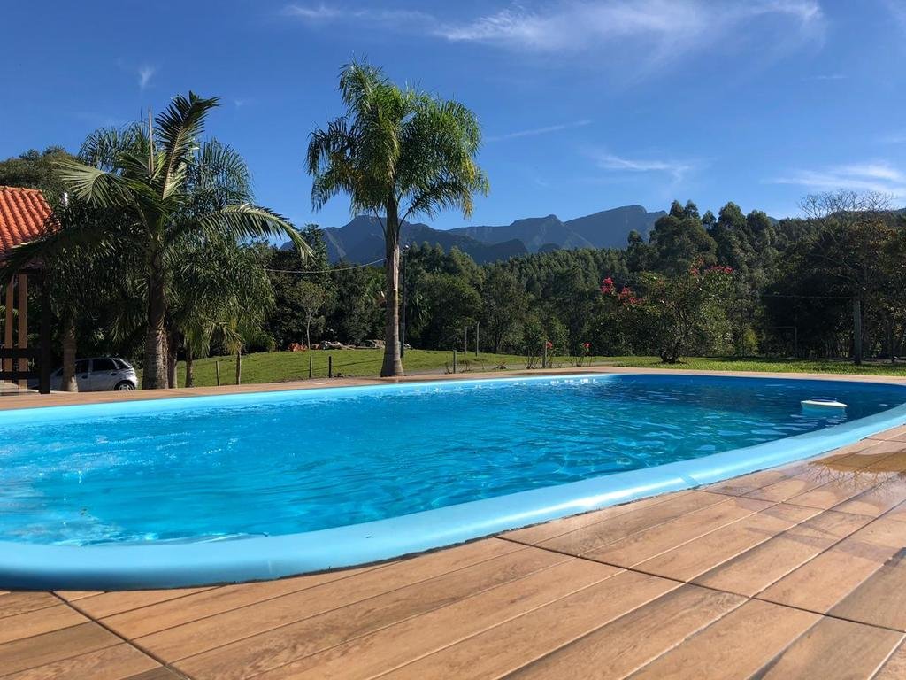 Piscina da Pousada Costão da Serra cercada por um gramado com árvores.