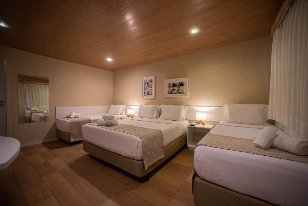 Quarto para quatro pessoas na Pousada da Germana, com uma cama de casal, e duas camas de solteiro, além de dois quadros decorativos, cortina e um espelho grande
