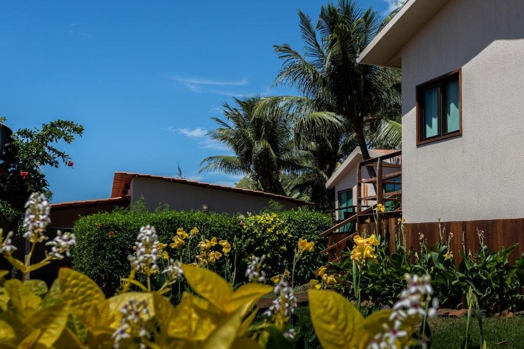 Parte da área externa da Pousada da Germana, em Fernando de Noronha, num dia de céu azul com poucas nuvens, e jardins floridos ao redor das hospedagens