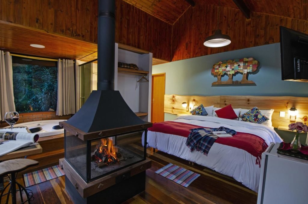 Pousada da Gruta em Visconde de Mauá. Há uma cama king de casal na direita da imagem. Na frente dela há uma lareira, que fica no meio do quarto. No canto esquerdo há uma banheira de hidromassagem.