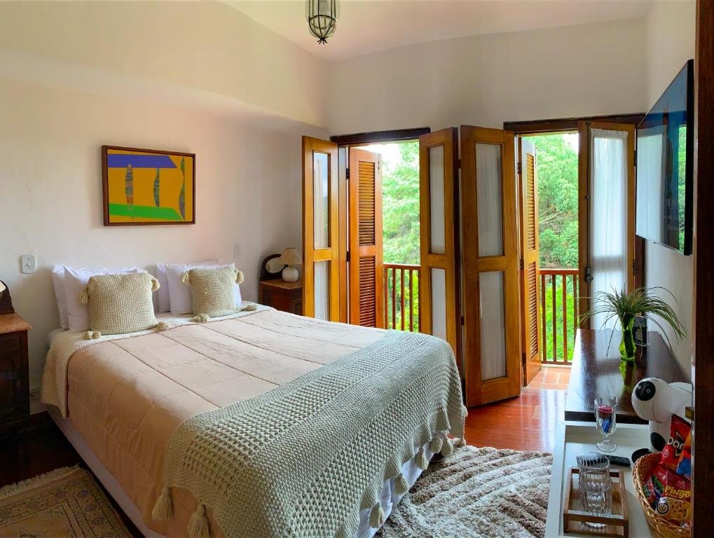 Quarto da Pousada Hortelã com uma sacada, cama de casal, uma televisão, um móvel de madeira, chão de madeira e um tapete