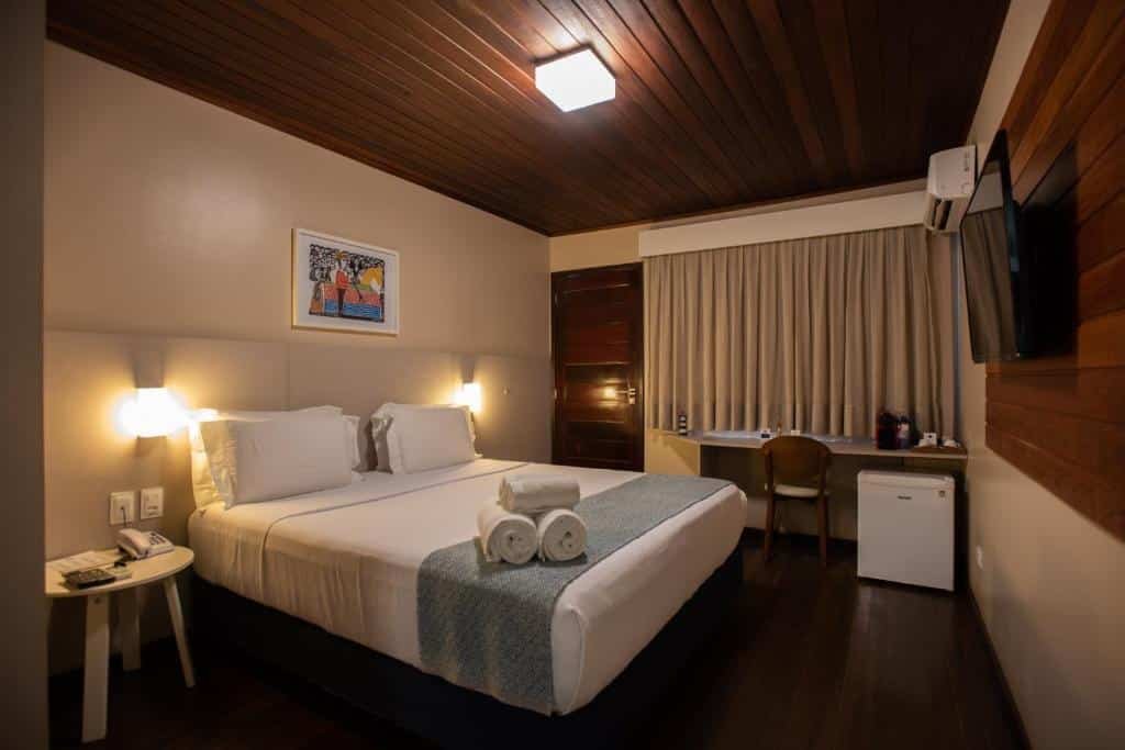 Quarto de casal da Pousada Lua Bela, com frigobar, ar-condicionado, TV, quadro decorativo na parede da cabeceira e mesinha com cafeteira