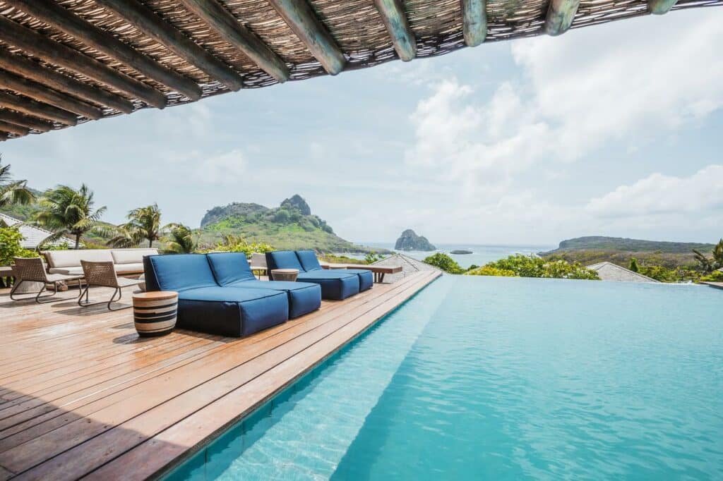 Piscina de borda infinita, com espreguiçadeiras azuis ao lado, no deck com vista para o mar, na Pousada Maravilha, em Fernando de Noronha