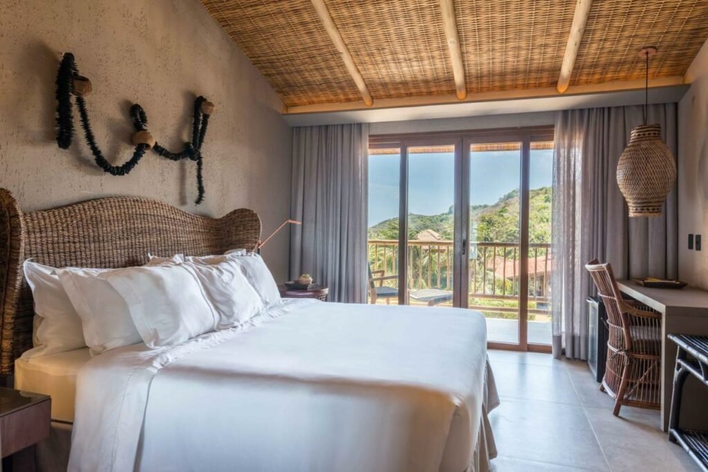 Quarto de casal na Pousada Maria Bonita Noronha, com cama ampla, sacada com vista, pendente sobre mesa e cadeira, tudo num estilo rústico chic