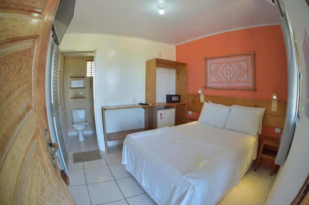 Quarto de casal em uma das pousadas em São Miguel dos Milagres, a Pousada Praia Bonita, onde há cama espaçosa, frigobar, cofre, TV na parede e uma porta aberta para o banheiro