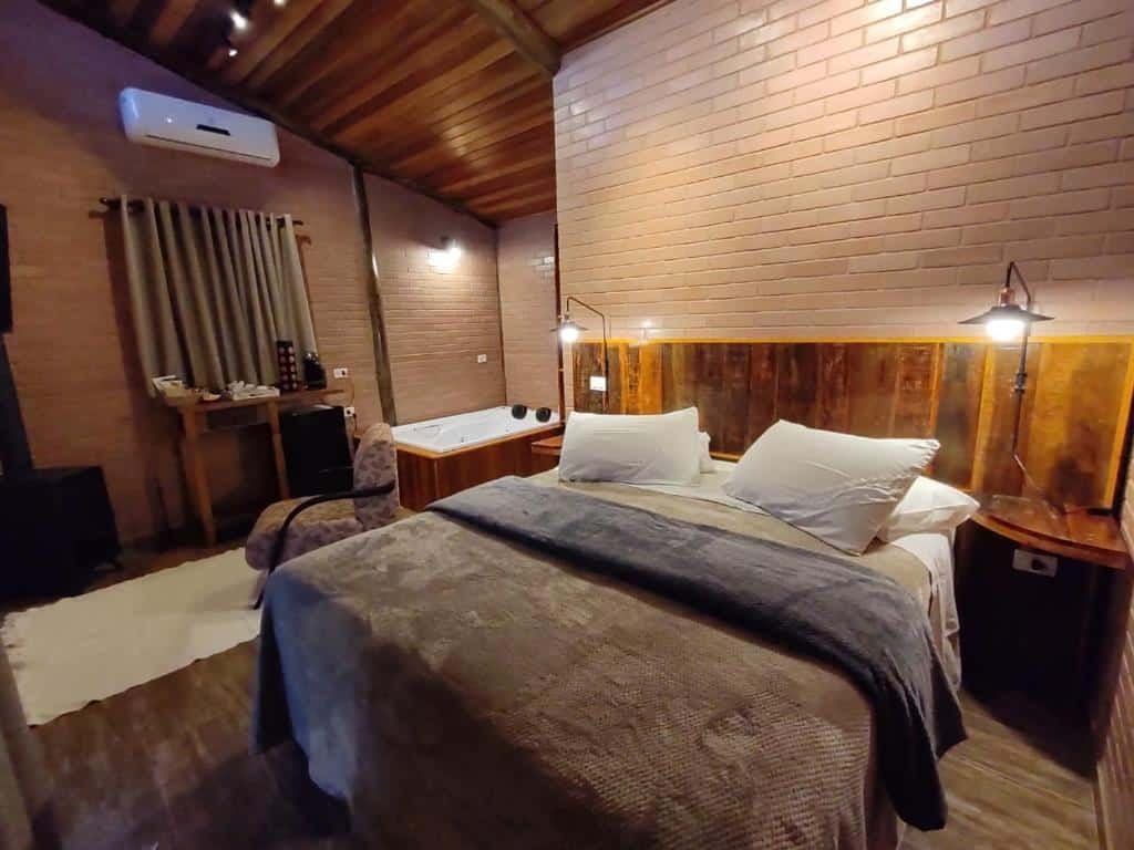 Quarto aconchegante do Pousada Recanto Primavera com cama de casal, detalhes em madeira, uma pequena banheira de hidromassagem, ar condicionado e uma escrivaninha com conjunto de café.