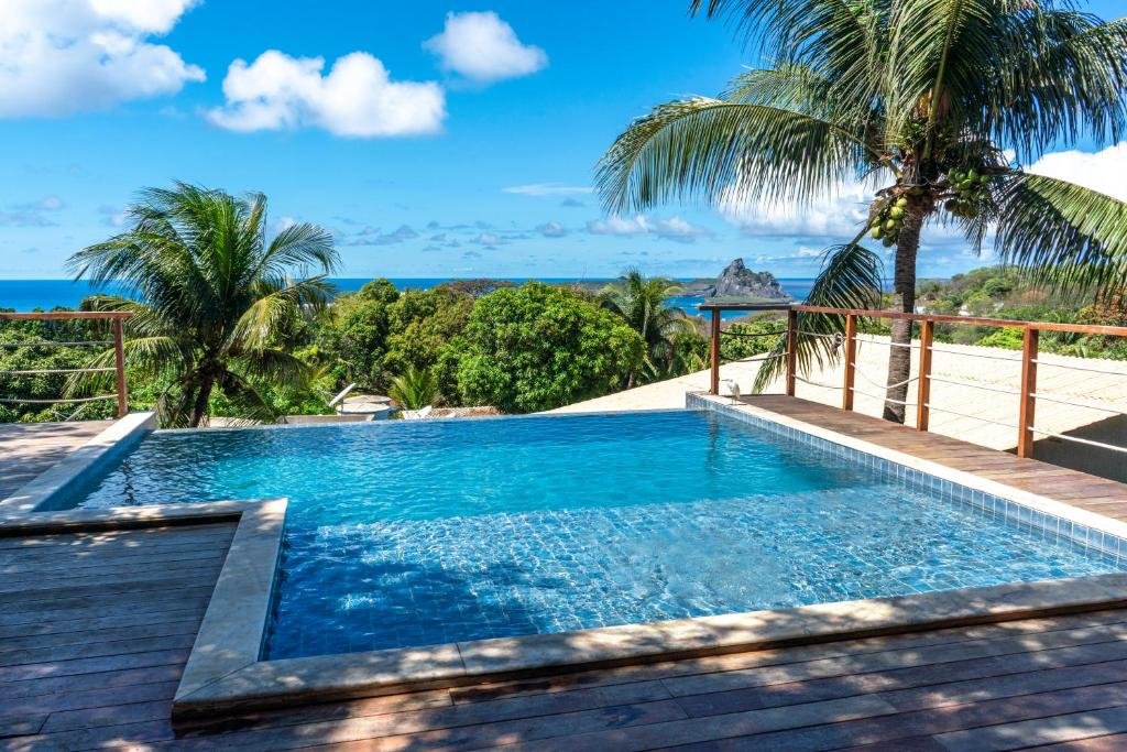 Piscina de borda infinita, com parapeito de madeira em ambos os lados, na Pousada Recanto, em Fernando de Noronha, inclusive com vista para o mar ao fundo e coqueiro ao lado