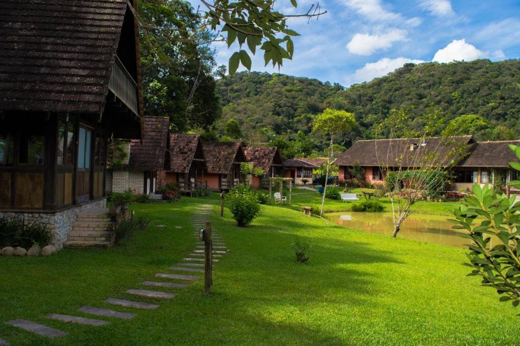 Chalés da Pousada Rio da Prata, localizado em um gramado verde cheio de vegetação em volta e um lado no meio durante um dia ensolarado