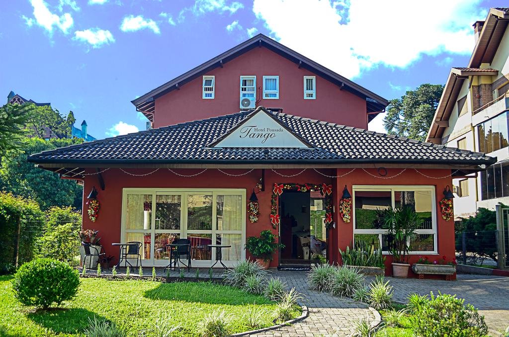 vista frontal da Pousada Tango em Gramado, uma construção de dois andares, com teto triangular e pintura vermelha. Na entrada é possível ver decorações natalinas