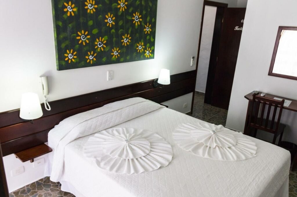 Quarto de casal com móveis de madeira escura e enxoval branco na Pousada Torre del Mar