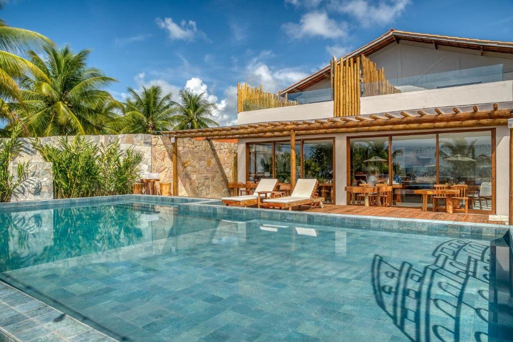 Piscina da Pousada Villa Italia,a com águas paradas, duas espreguiçadeiras ao fundo, mesinhas e portas de vidro para entrada no espaço interno da propriedade
