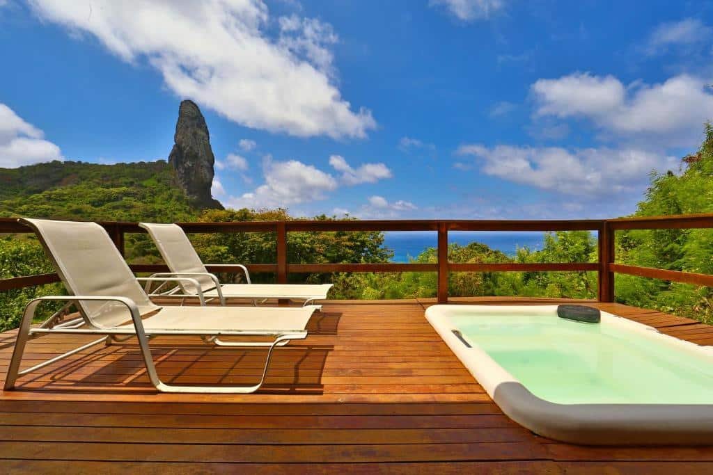 Deck de madeira, com duas espreguiçadeiras em frente a uma banheira de hidromassagem, e vista para a natureza e o mar de Fernando de Noronha, na Pousada Zé Maria