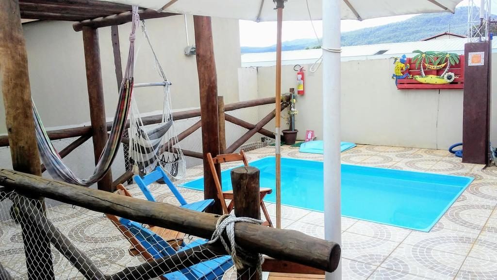 Área da Piscina da Pousada Zoe, com pequena piscina ao centro e ao entorno balanço e rede e chão de piso e guarda sol ao canto. 