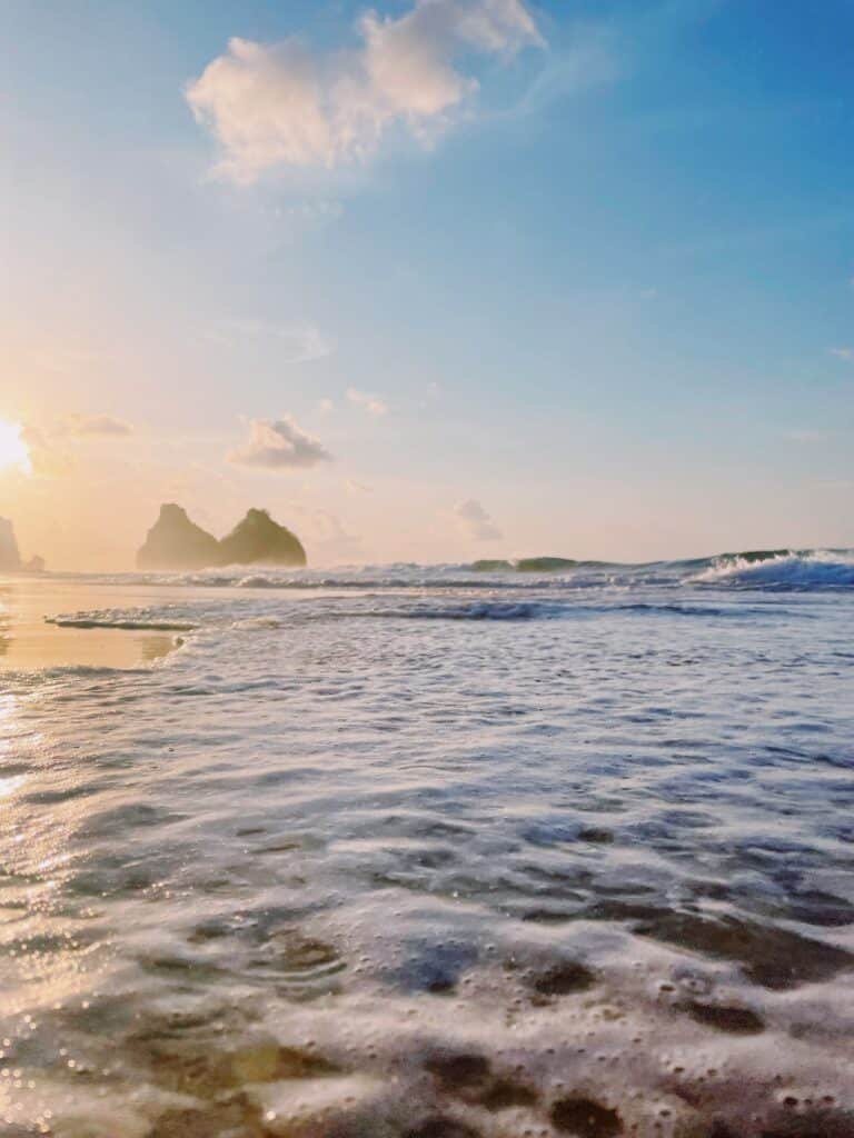 Mar em frente ao Morro Dois Irmãos, visto ao fundo, em um dia de céu azul, ao entardecer, ilustrando o post de pousadas em Fernando de Noronha