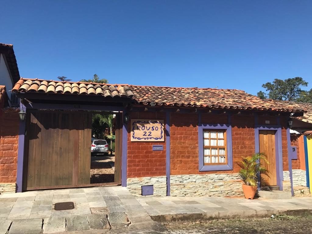 Fachada da Pousada Pouso 22 de pousadas em Pirenópolis. Fachada rústica de tijolos com duas portas e uma janela, calçada de pedras e uma placa com o nome da pousada. 