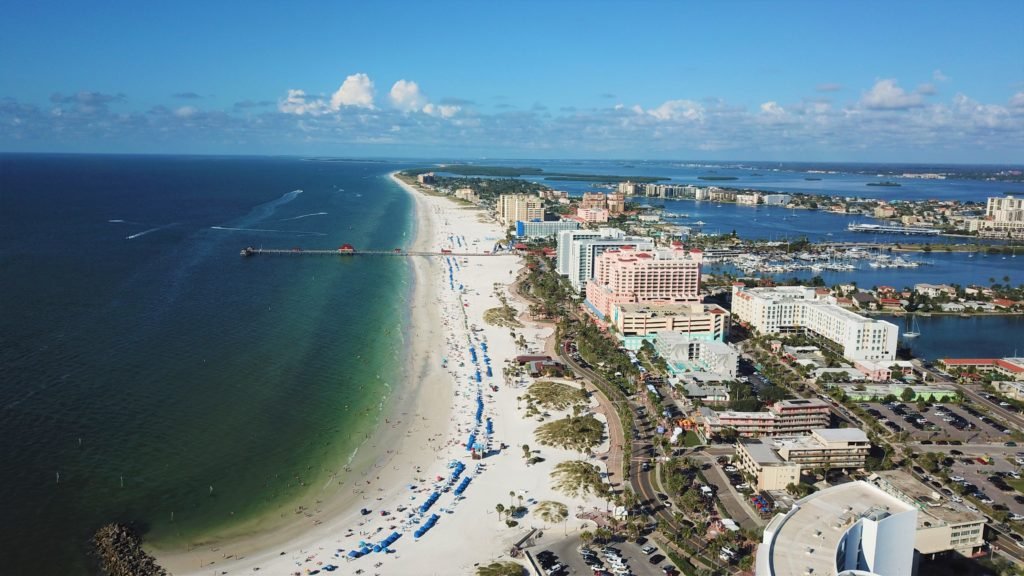 Praia de Clearwater em visão panorâmica, estando o mar à esquerda, a orla da praia quase ao centro da foto, e prédios ao lado direito