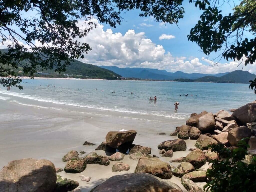 Praia das Toninhas em Ubatuba com muitas pedras e algumas árvores na extensão ampla de areia e o mar calmo