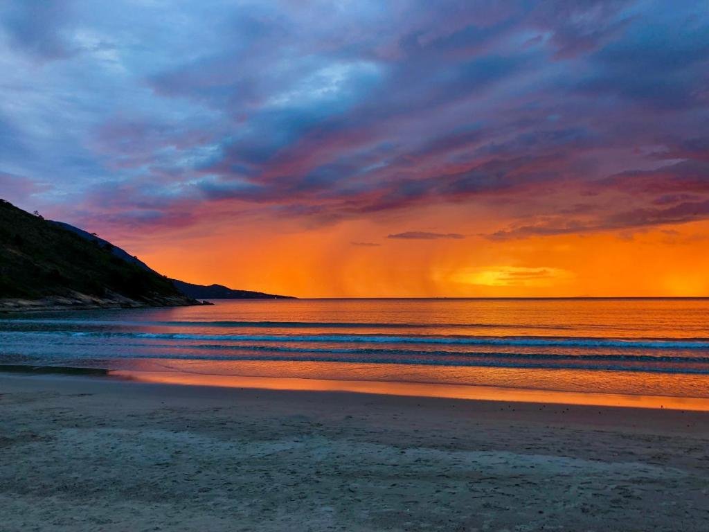 Vista do por do Sol da praia de Guaecá, em São Sebastião com areia a frente e ao fundo o mar.