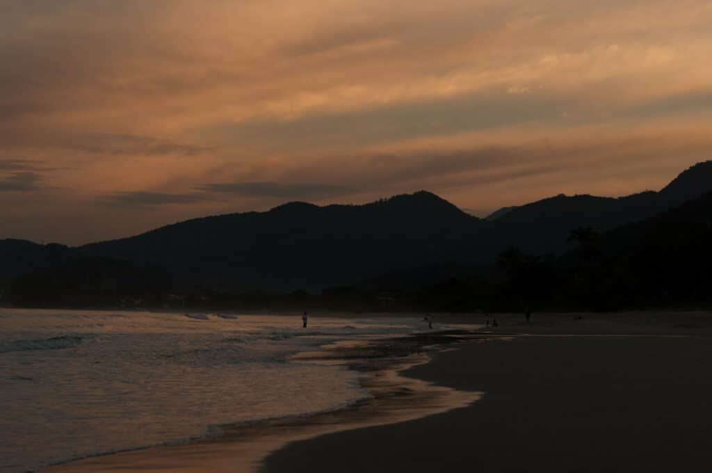 Praia de Lagoinha em Ubatuba durante o final do dia com a praia a frente com areia do lado direito da imagem e do lado esquerdo o mar ao fundo algumas pessoas na faixa de areia.