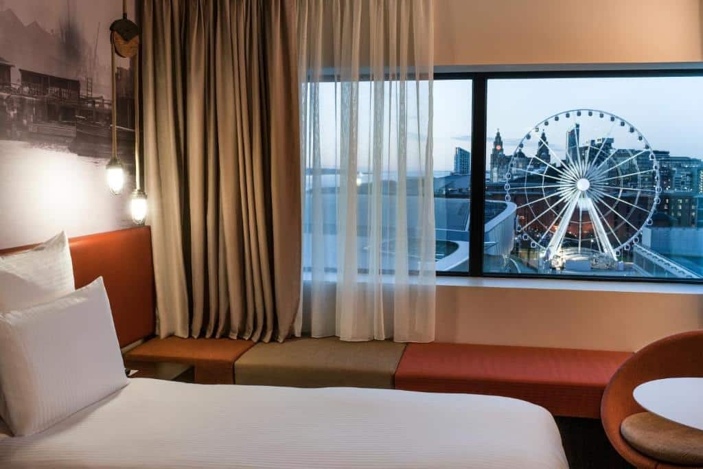 Quarto do Pullman Liverpool, aparecendo parte da cama, e janela com vista da rua e roda gigante