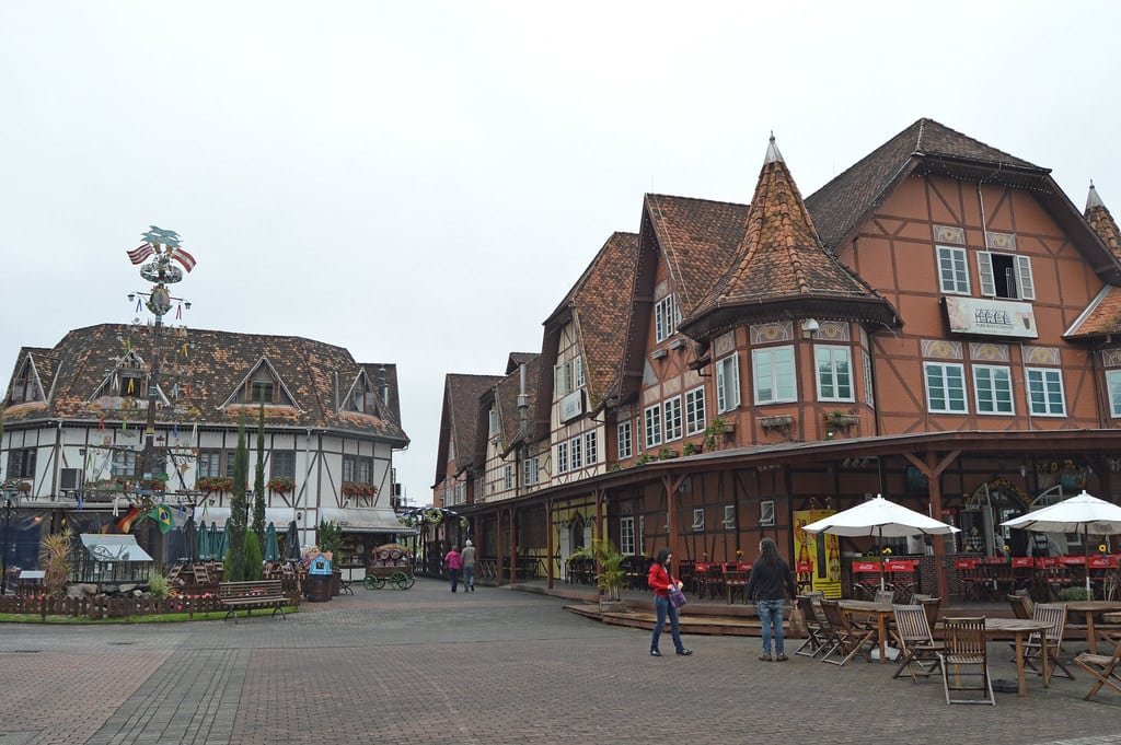 Centro histórico com edifícios com estrutura de madeira e telhados íngremes, mesas ao ar livre e alguns pedestres em um dia nublado.