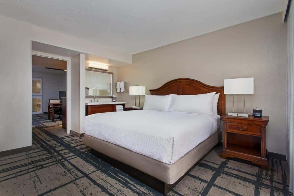 quarto com cama de casal com mesinhas e luminárias de ambos os lados, lavabo e um outro ambiente com mesa e cadeiras no Embassy Suites by Hilton Orlando International Drive Convention Center