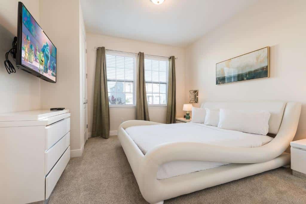 quarto do Fabulous Home Near Disney com uma cama de design diferentão mais baixa em branco com tv e cômoda também branca em baixo, há uma janela grande dividida em duas com cortinas um pouco mais escuras em um ambiente de tamanho ok no Fabulous Home Near Disney