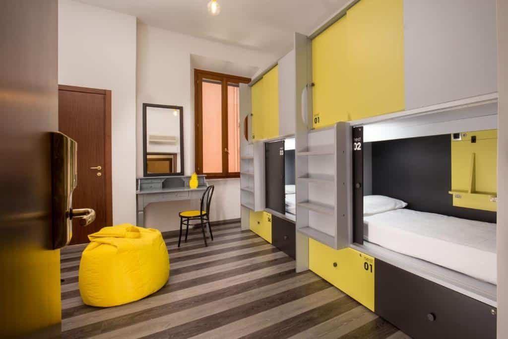 quarto do Free Hostels Roma, um dos hostels em Roma, com puff amarelo, escrivaninha e beliches com camas e portinhas que é possível trancar