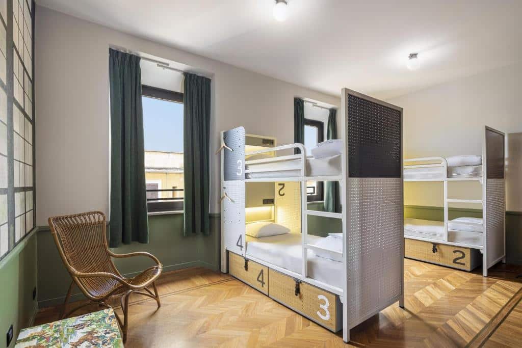 quarto do Generator Rome, um dos hostels em Roma, duas beliches com lugar para guardar itens e escada, há mesa com cadeira e duas janelas grandes com cortinas