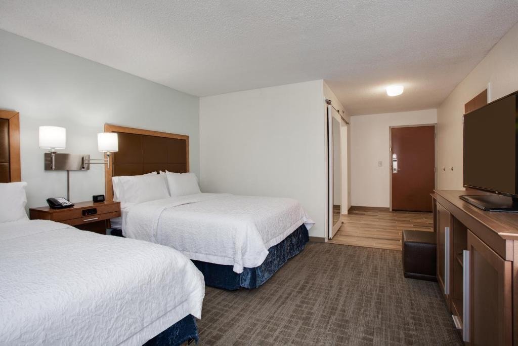 quarto amplo com duas camas de casal, mesinha e luminária dos lados, tv e balcão à frente e uma entrada grande que dá para o banheiro do Hampton Inn Orlando-Convention Center