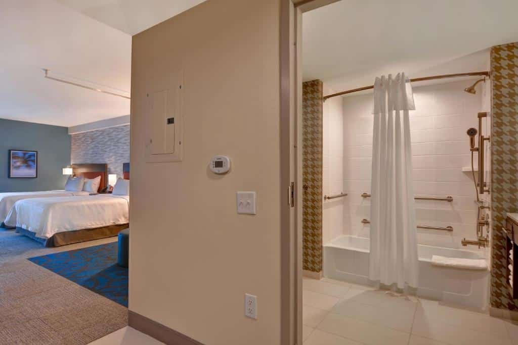 quarto com cama de casal bem espaçoso com banheiro acessível com barras de apoio, cortina de tecido e chuveiro adaptado no Home2 Suites By Hilton Orlando Flamingo Crossings, FL