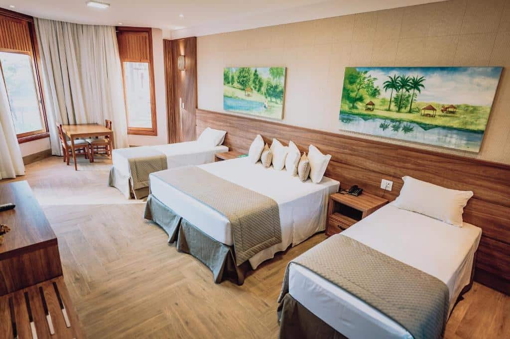 Um espaçoso quarto do Hotel Fazenda Salto Grande com uma cama de casal, duas camas de solteiro, detalhes em madeira, pinturas na parede e uma pequena escrivaninha perto da janela.