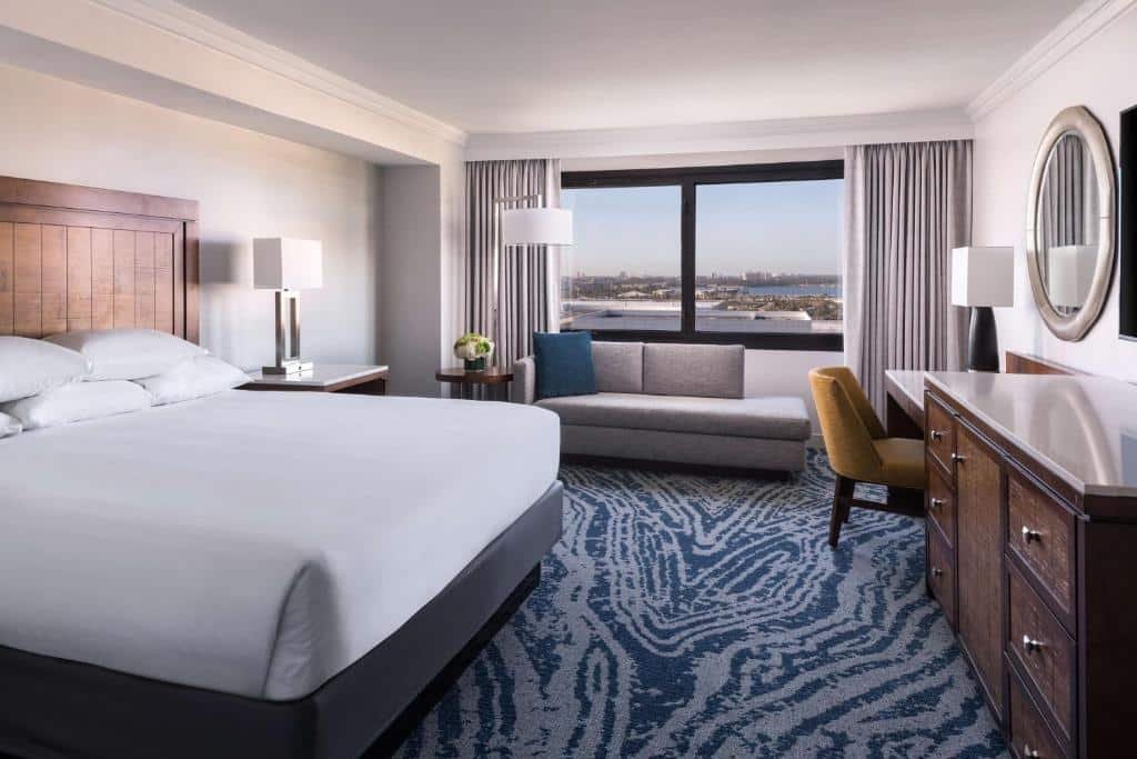 quarto com cama grande, mesa de trabalho, sofá, cadeira, janela grande com vista para a baía e carpete em tons de azul marmorizado do Hyatt Regency Orlando, um dos hotéis em Orlando