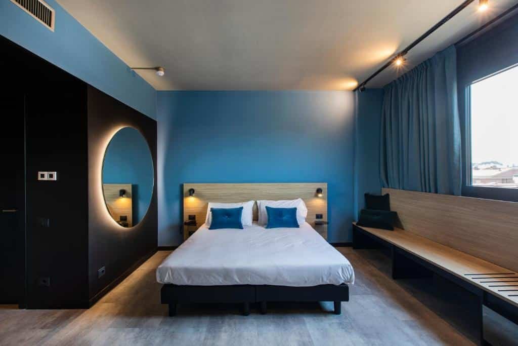 quarto amplo do Ibis Styles Roma Aurelia com cama de casal, sofá embutido embaixo da janela com vista e, do outro lado, um espelho redondo