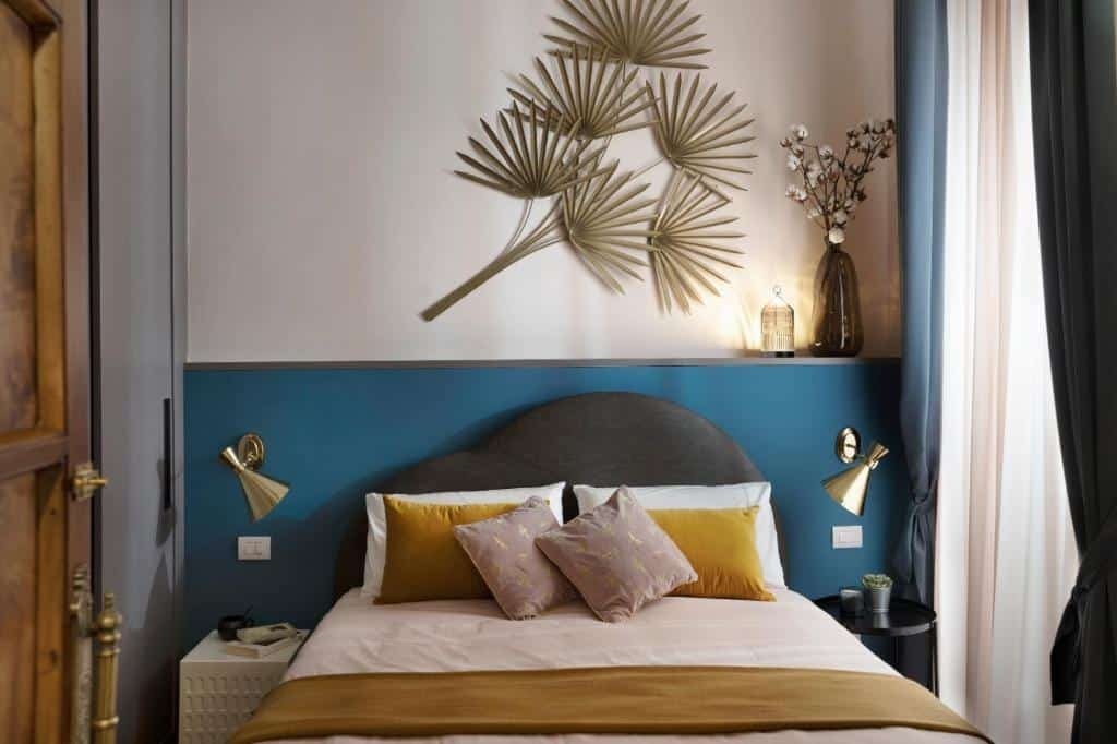 quarto do Luxury Trevi House, uma das opções de onde ficar me Roma, com cama de casal, luminárias em cima da mesinha de cabeceira de ambos os lados, há decoração na parede e vasos de plantas, há uma janela de um lado com cortinas e, do outro, um guarda-roupa