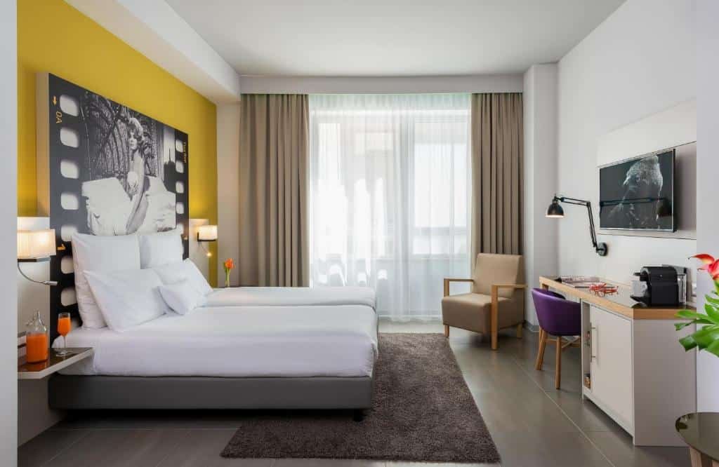 quarto com cama e janela grandes, tv e parede e poltrona amarelas no NYX Hotel Milan by Leonardo Hotels