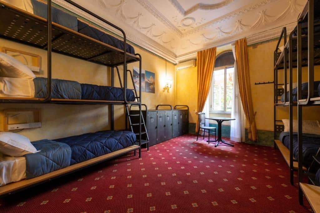 quarto do Ostello Bello Roma Colosseo, um dos hostels em Roma, com duas triliches, armários com chave, mesinha com cadeira e janela com cortinas, há uma decoração clássica no local