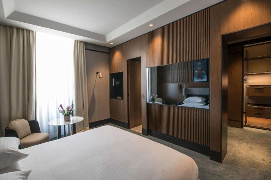 quarto do Umiltà 36, um dos hotéis de luxo em Roma, com cama de casal e tv em frente com mesinha e cadeira ao lado e uma entrada para uma salinha de estar ao fundo
