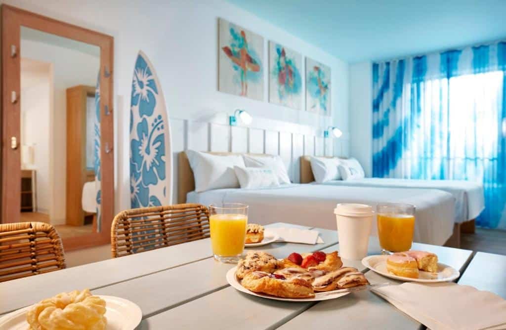 quarto com café da amnhã posto na mesa com cadeiras e decoração de surfem com cama de casal com luminárias acima do Universal