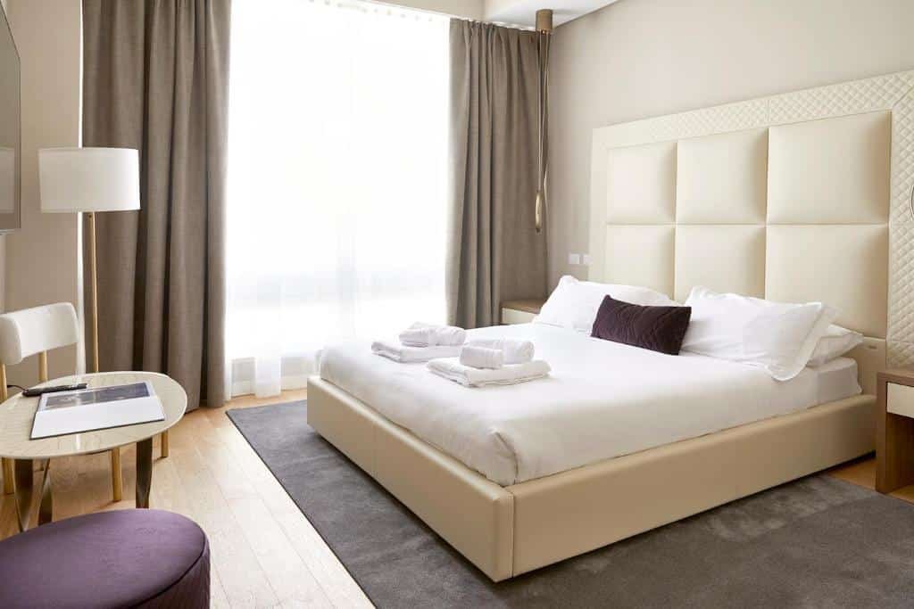 quarto com cama bem grande e cabeceira com detalhes brancos e janela grande com cortina, balcão e tv do PRESTIGE BOUTIQUE APARTHOTEL -Piazza Duomo em Milão